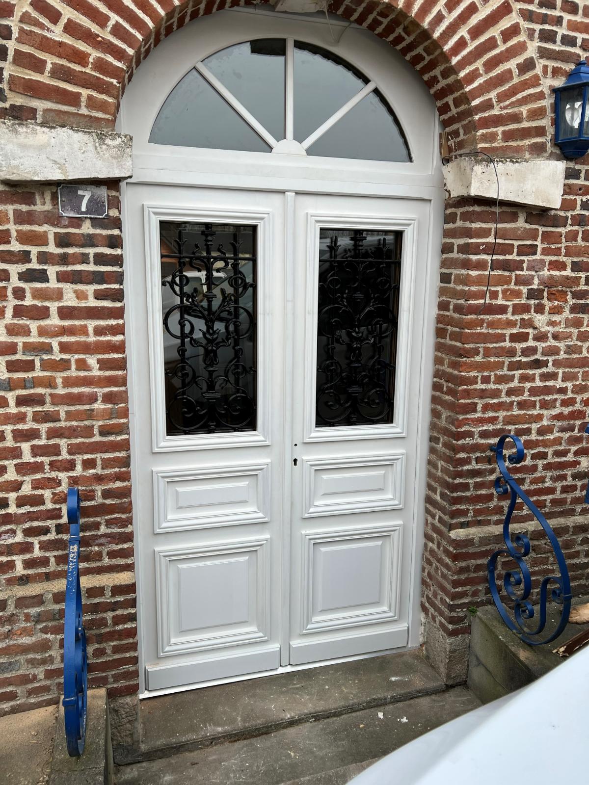 Porte blanche avec des fenêtres latérales et un balai bleu posé contre le mur