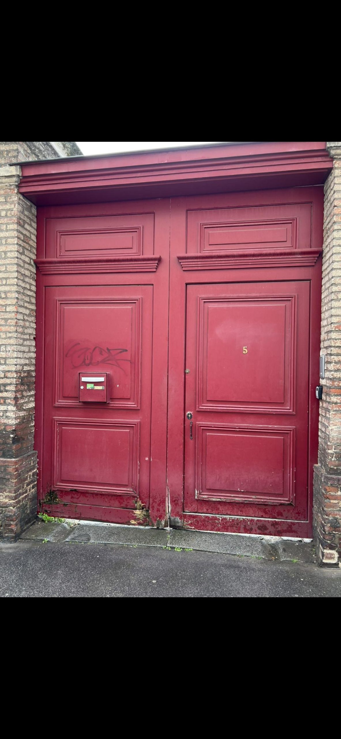 Une porte rouge en bois avec une boîte aux lettres intégrée.